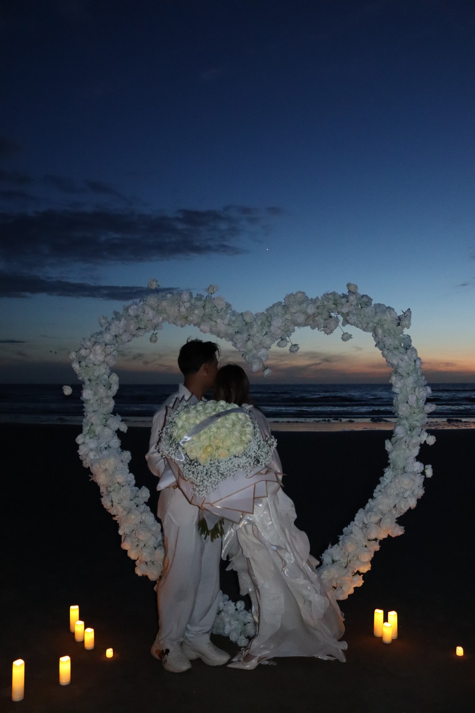 Rozenhart van Lumors — hartvormige bloemenboog met LED-kaarsen op het strand bij zonsondergang